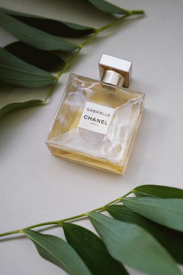 Gabrielle perfume bottle lying on a table and surrounded by leaves